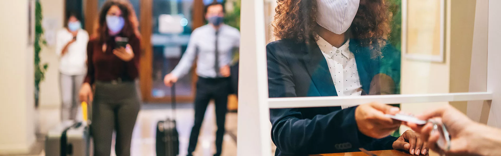 Hotel guests wearing protective face masks and social distancing in front of the hotel reception Gruppenreise